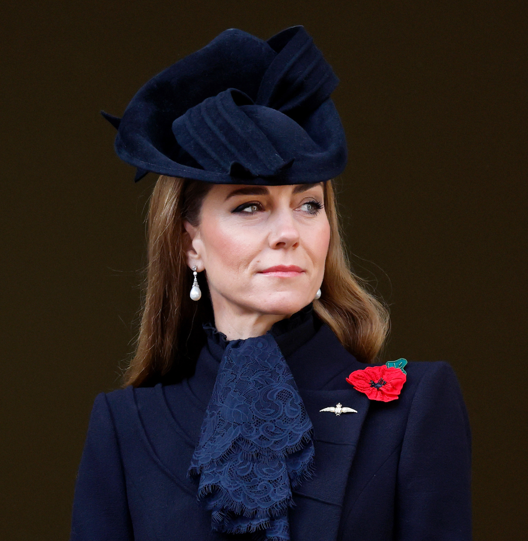 Kate Middleton wearing a black coat and hat with a red poppy pin