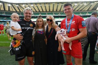 Owen Farrell holding a baby while stood next to his wife in a rugby stadium