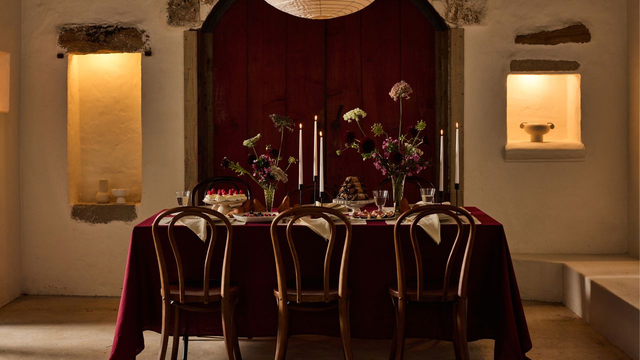 Images of a moody, Christmas dining table. There is a deep red table clothes, white napkins, and white candle sticks. 