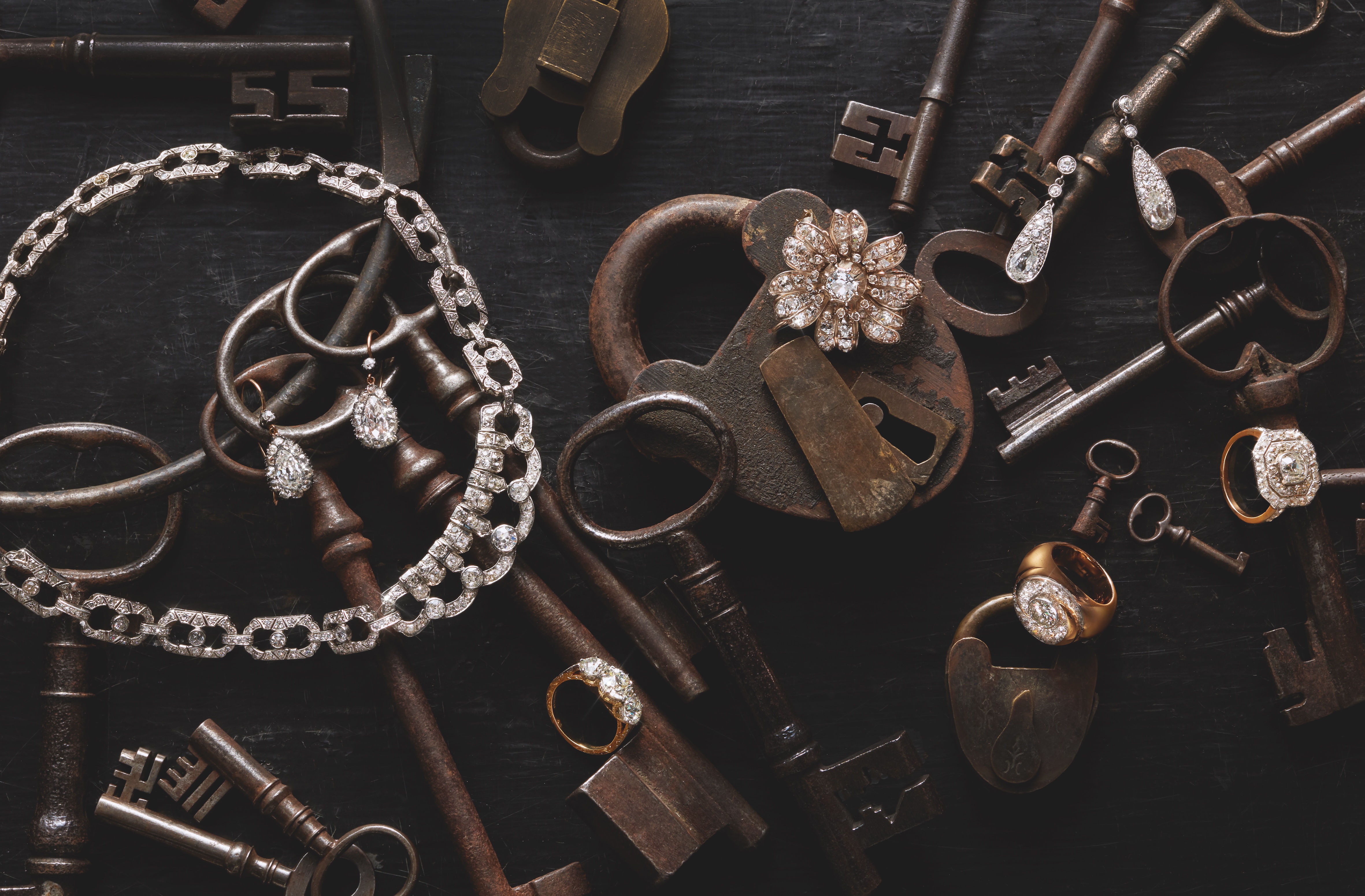 Flatlay of diamond jewellery arranged on old keys and padlocks 