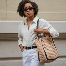 Ellie Delphine wears a full Mango look, sunglasses, golden earrings, a white linen shirt, a black leather belt with golden buckle, golden bracelets, a white ripped denim shorts, a large brown raffia bag, during a street style fashion photo session, on May 08, 2024 in Paris, France. 