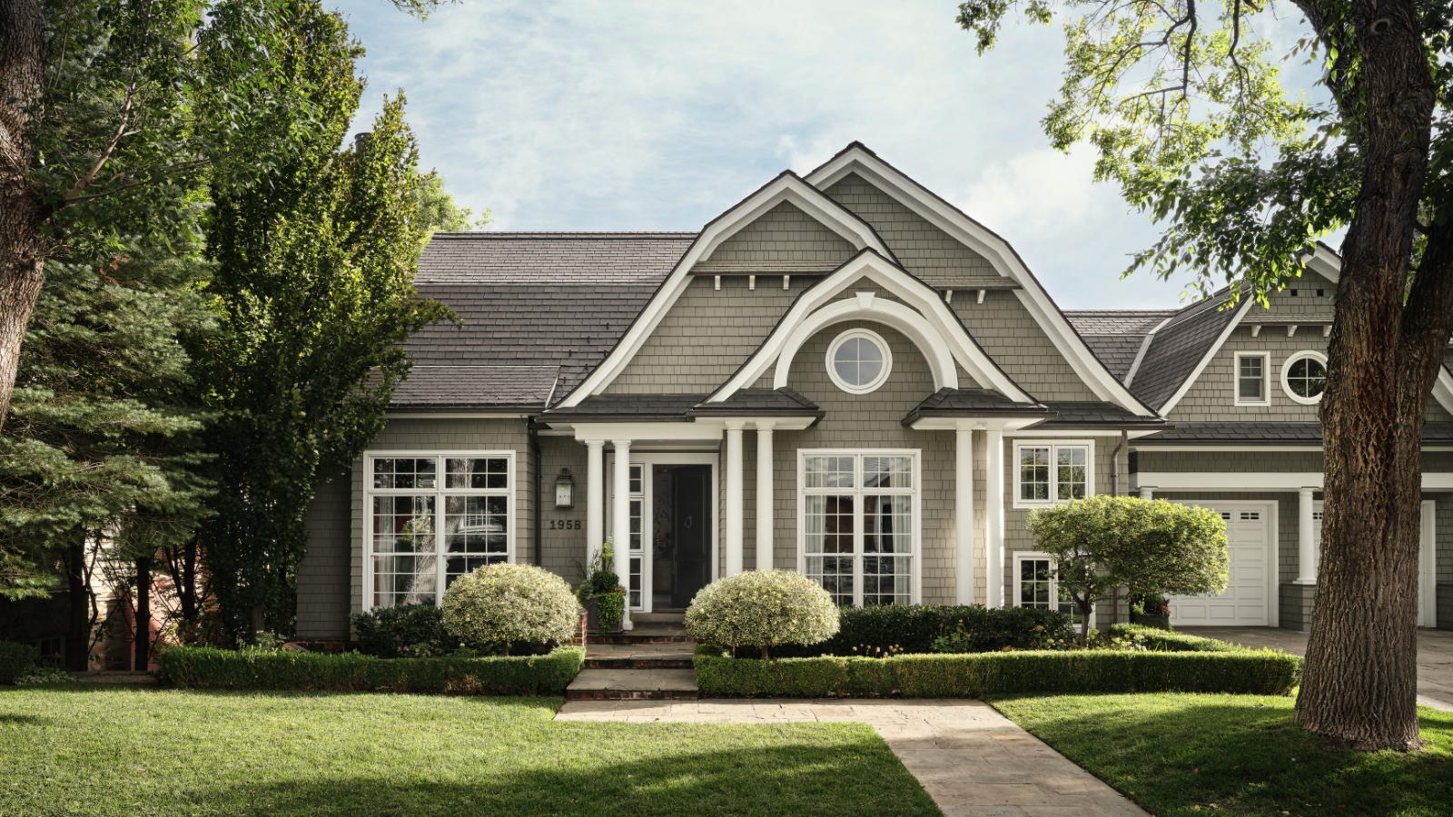 Gray shingle-style Salt Lake City home with white trim, curved gables and a tree-framed front lawn.