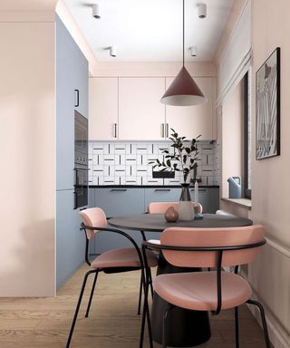 A dining area in a small kitchen with rounded black table, pink and black chairs, pink cone-shaped pendant light, monochrome wall art, and black and white graphic tiles