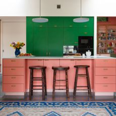 Pink and green kitchen with wooden bar stools and a blue rug