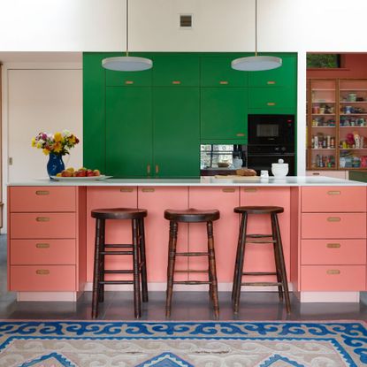 Pink and green kitchen with wooden bar stools and a blue rug