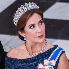 Queen Mary of Denmark looking to the side while wearing a blue sequined top and sash with a diamond necklace and diamond and pearl tiara