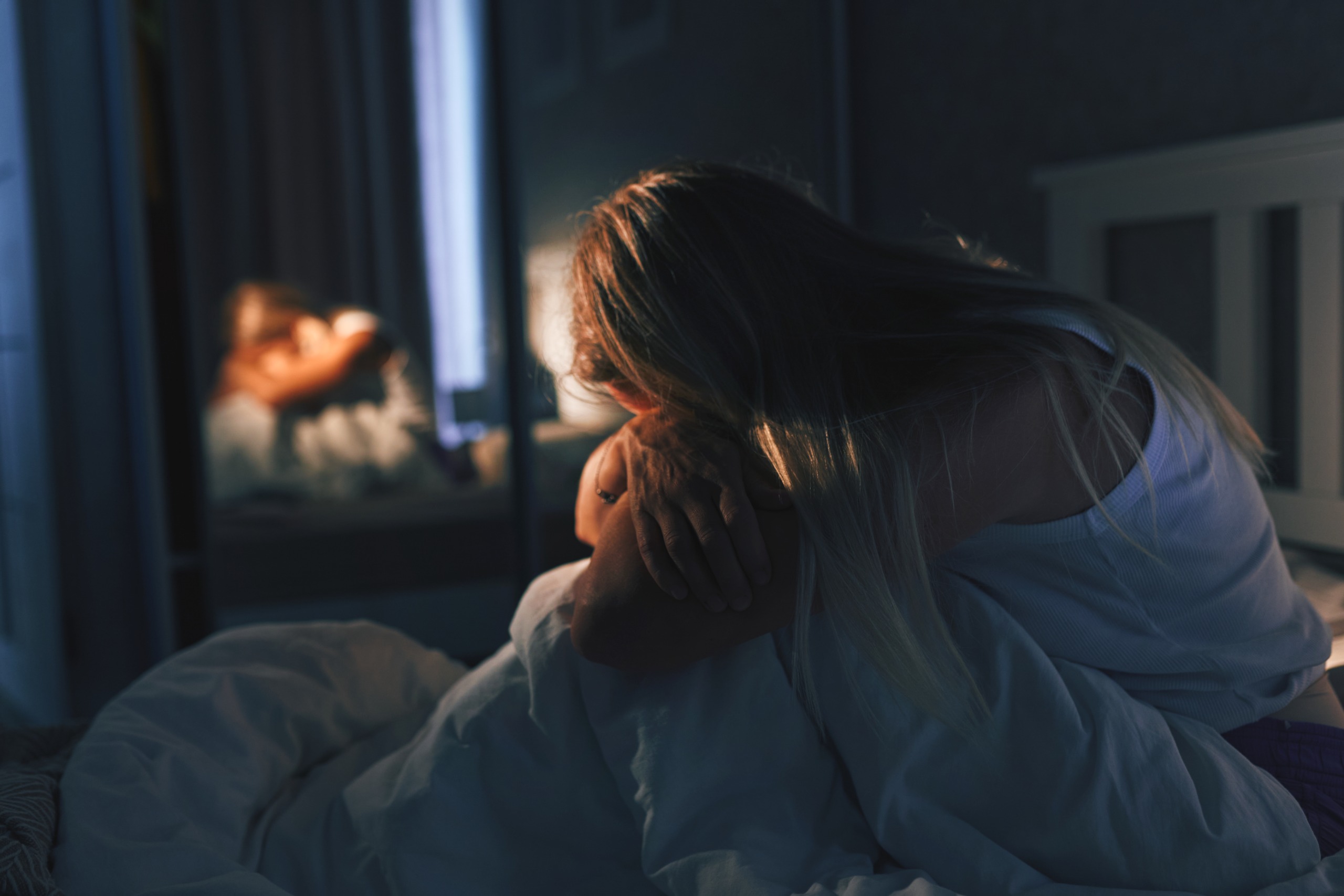 A woman sits up in bed at night with her head on her arms, appearing stressed.