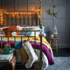 a bed covered in colourful bedding with a Christmas stocking, a mini Christmas tree and fairy lights