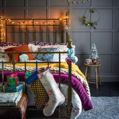 a bed covered in colourful bedding with a Christmas stocking, a mini Christmas tree and fairy lights