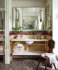 A Mediterranean bathroom with a gold and marble vanity, tiled mosaic floor, zellige tiles in beige and burgundy on the walls, and a large vanity mirror
