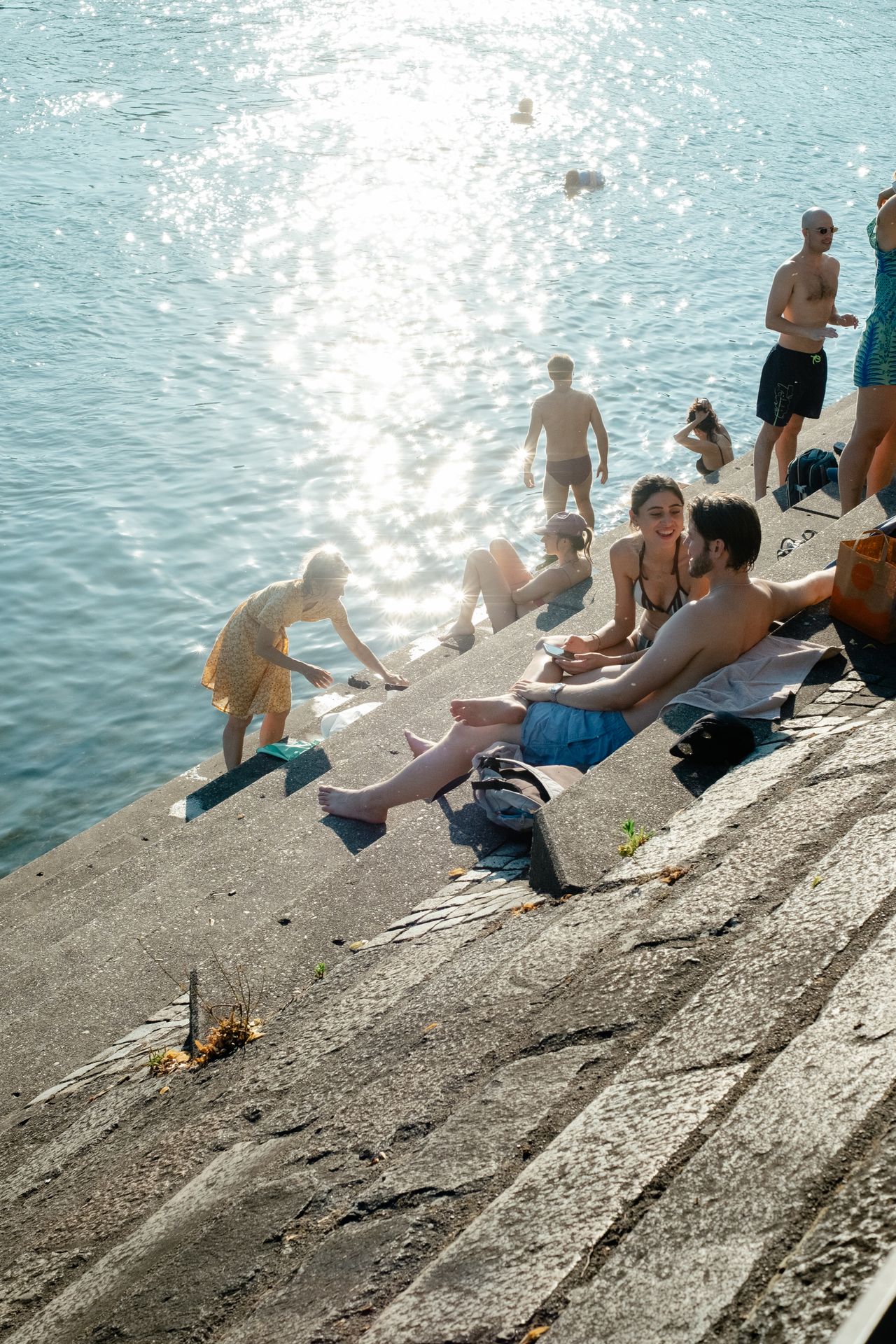A series of lifestyle images depict people at leisure and play in a Swiss town bathing in sunshine, whether enjoying the weather near the river bank or abstract painting murals at an art fair.