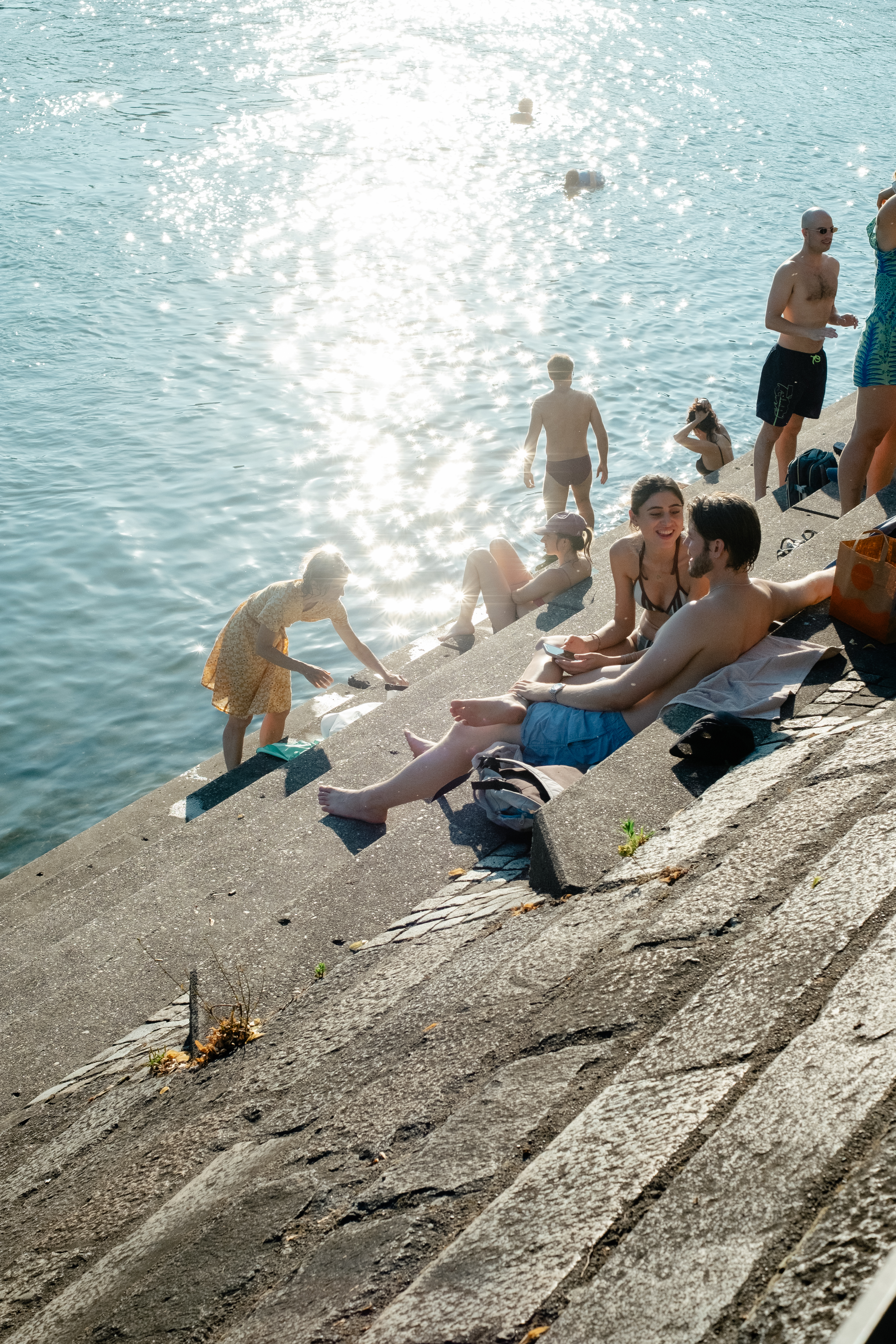 A series of lifestyle images depict people at leisure and play in a Swiss town bathing in sunshine, whether enjoying the weather near the river bank or abstract painting murals at an art fair.