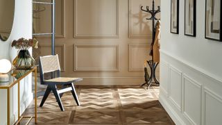 An elegant hallway featuring classic wall paneling in soft neutral tones, complemented by a geometric wooden parquet floor. 