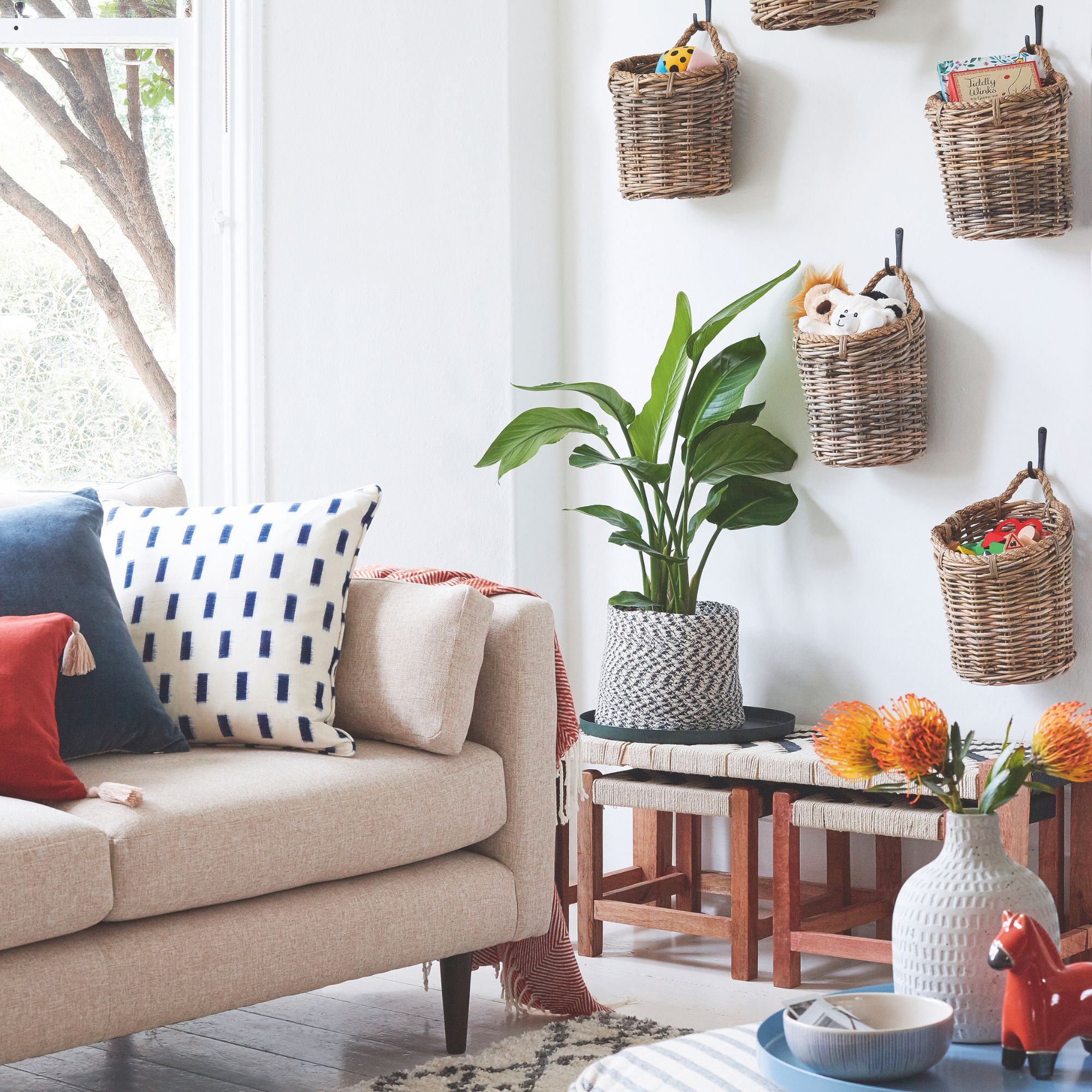 White living room with a pink sofa and wicker baskets hanging on the wall