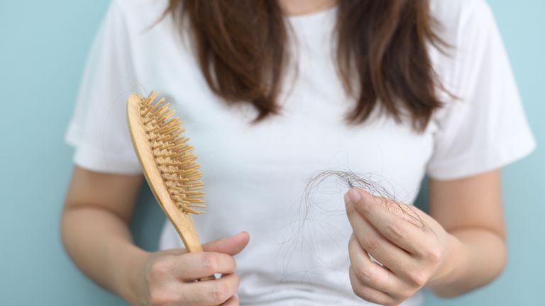 woman holding hairbrush with loose strands, meant to symbolize can birth control cause hair loss