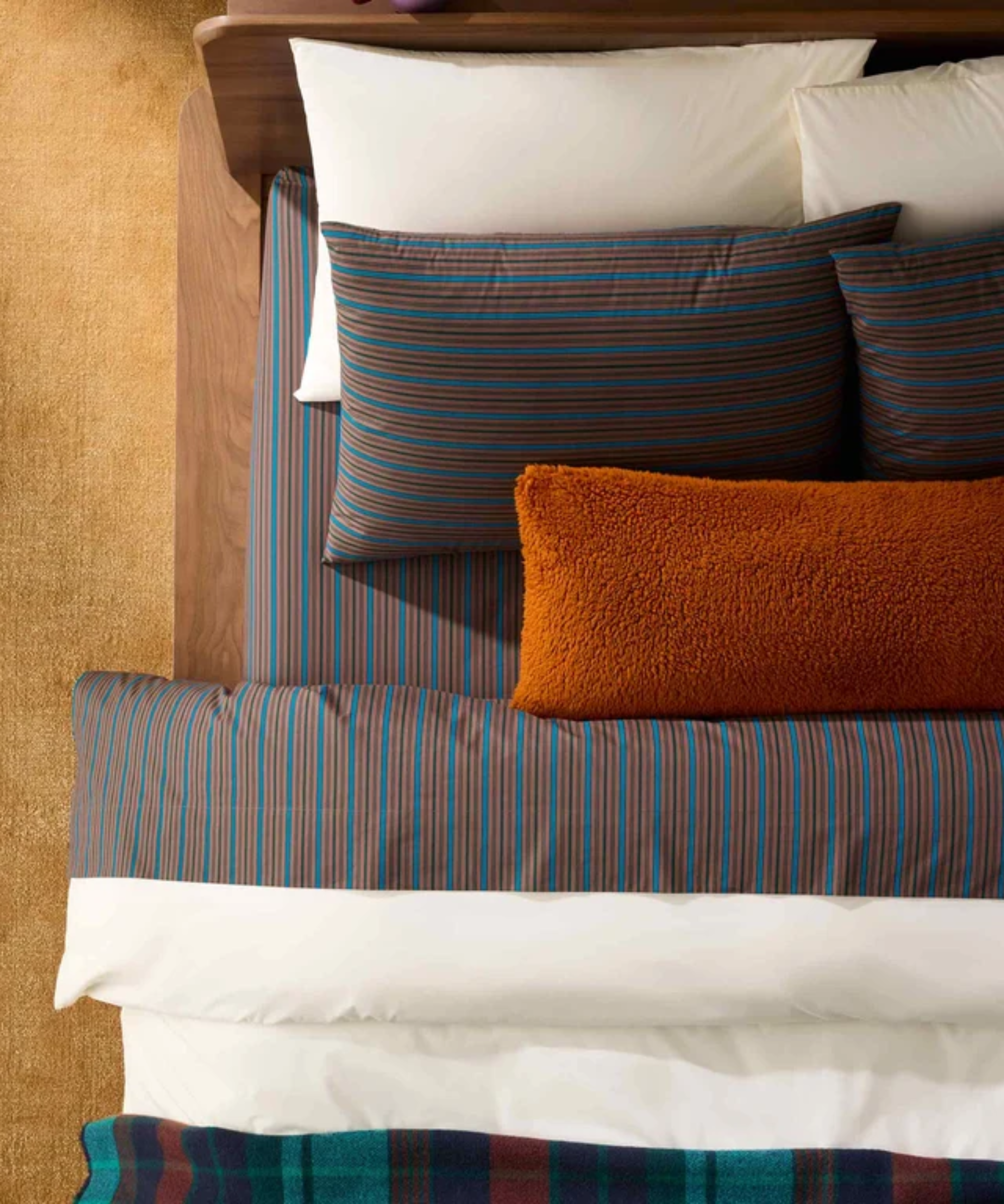 Bird's-eye bedscape view of layered striped sheets, fluffy throw pillows, and a plaid coverlet.