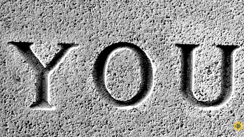 Close-up, black and white image of the word &#039;YOU&#039; carved into a rough, grainy stone surface, resembling a tombstone or ancient monument