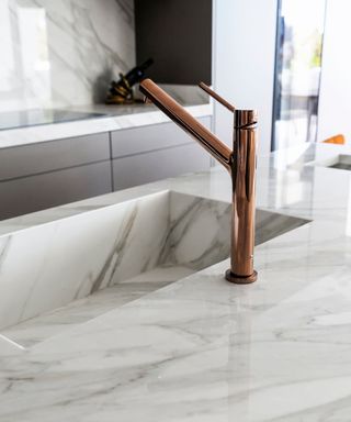 A sleek, contemporary kitchen sink with a marble worktop, integrated basin and a rose gold tap.