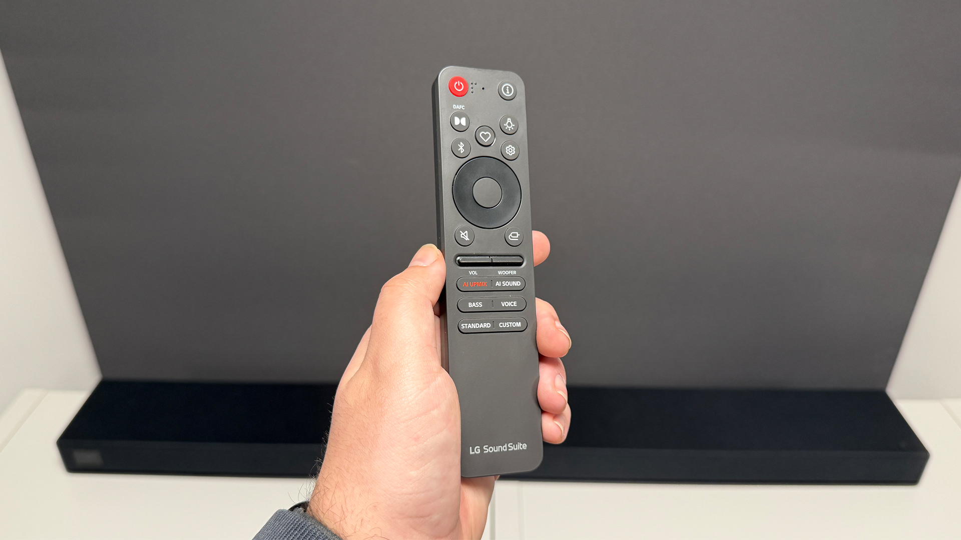 LG Sound Suite H7 soundbar remote control held in hand above soundbar