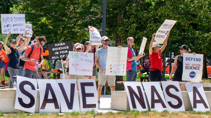 People hold signs outside on a sunny day in protest of NASA budget cuts, July 20, 2025.