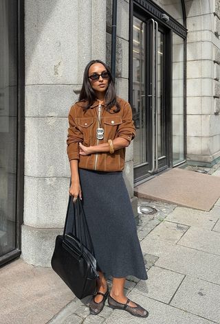 best womens shackets shown on a woman standing in the street wearing a suede jacket with a gray skirt, mesh ballet flats, and a black bag