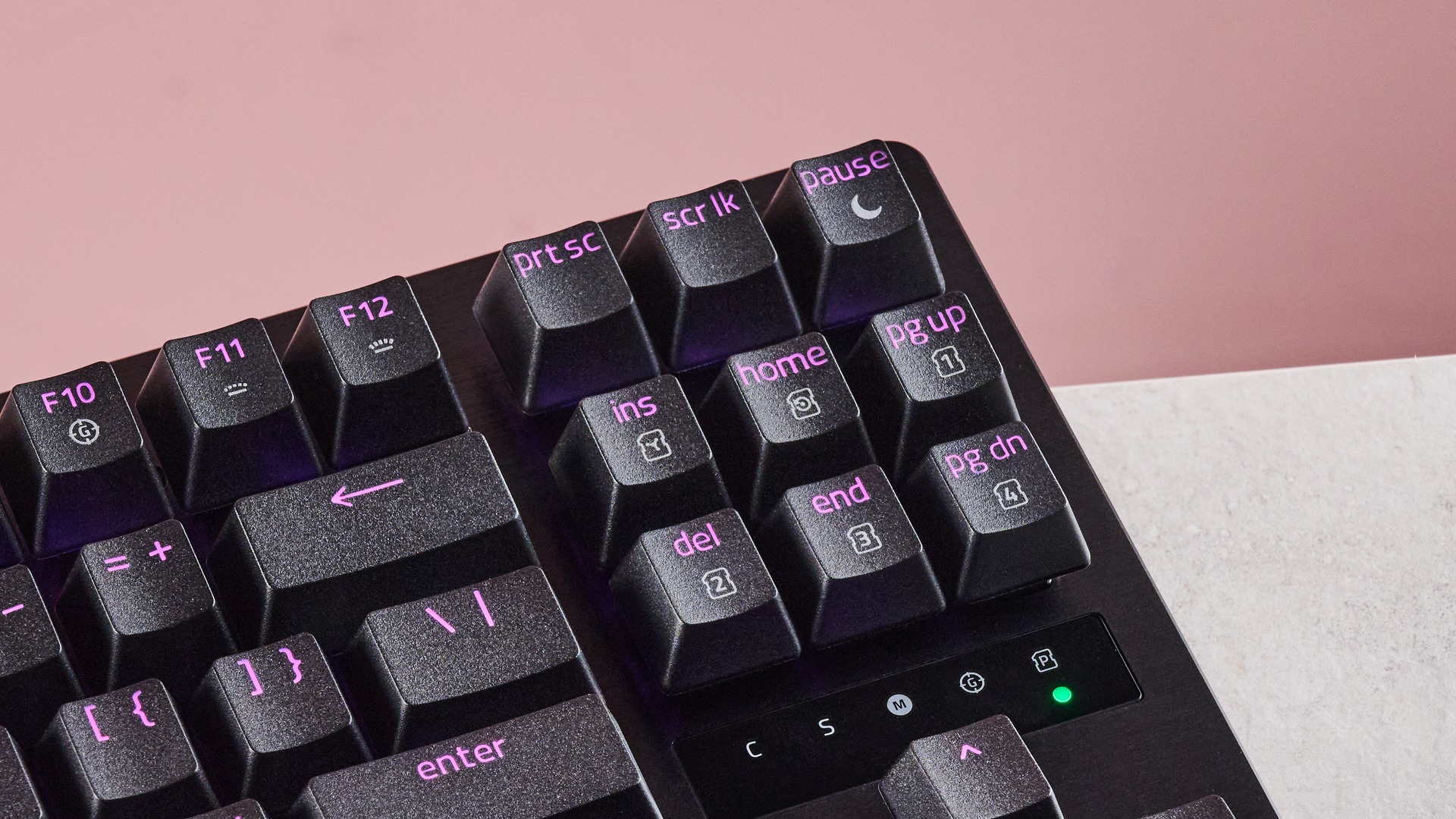 Close-up of top-right keys on Razer Huntsman V3 Tenkeyless 8KHz, with purple RGB backlighting, on a desk with pink wall in background