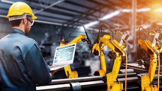Man standing in front of manufacturing machinery with laptop