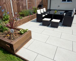 Clean concrete patio with table and chairs in centre and raised wooden plant section on the border