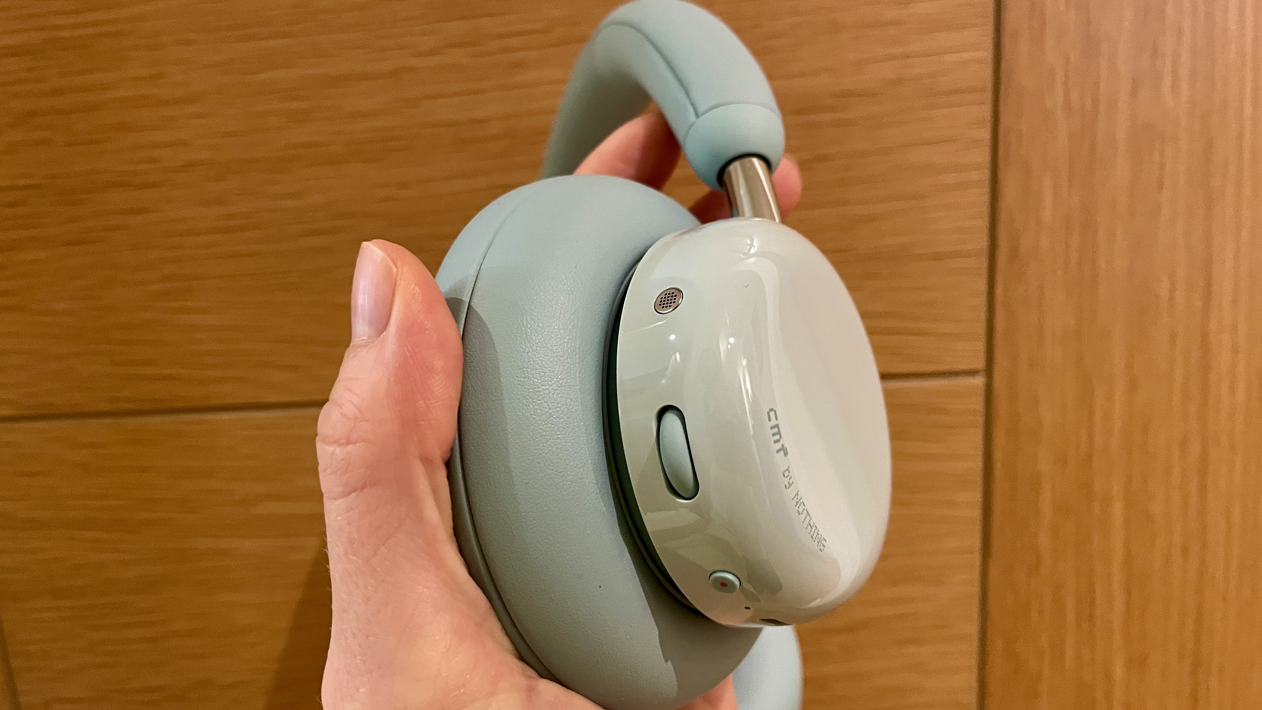 CMF Headphone Pro in pistachio green held in a hand or hung on a barbell, being pushed up by a carved frog