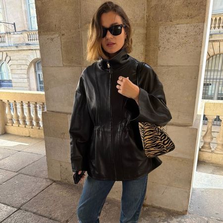 Influencer @annelauremais wears a black leather jacket with blue jeans, white heeled shoes and a tiger print bag.