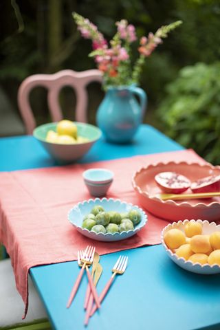 garden dining table painted bright blue and covered with a pink table runner