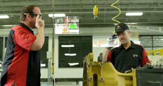 Two factory workers interact with machinery using Goolge Glass headsets.