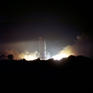 A Saturn V rocket launches Apollo 17. It is night but the energy from the launch lights up the scene.