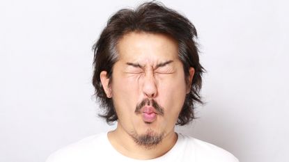 A man puckers up his face as if tasting something sour.