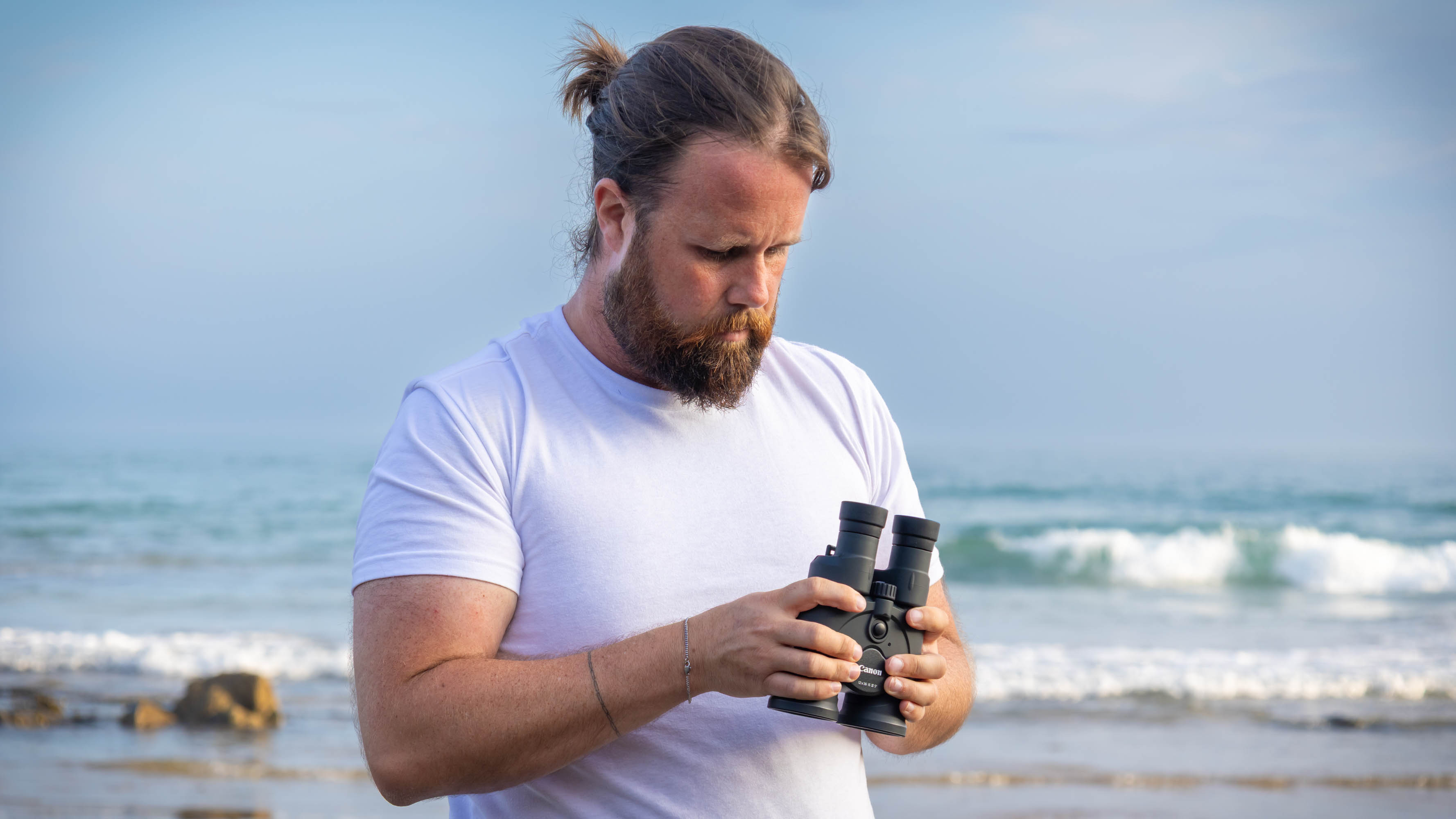 A male standing next to the sea holding the Canon 12x36 IS binoculars.