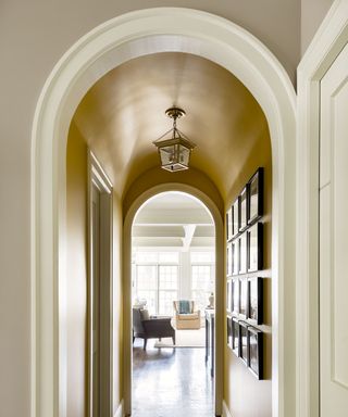 A barrel vaulted hallway painted yellow up to the ceiling, with gallery wall and living room in the background.