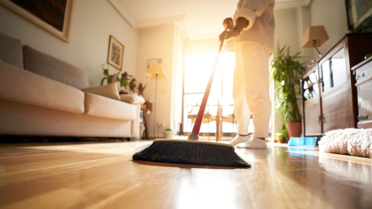 Woman sweeping a living room floor with sun setting in background