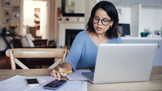 A woman sitting with a laptop and calculator manages her freelance finance 