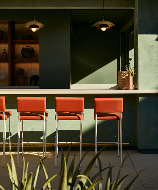 Burn orange, mid-century-style stools in green-colored outdoor bar area