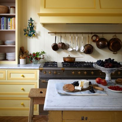 Yellow kitchen with copper pans hanging over range cooker from a rail