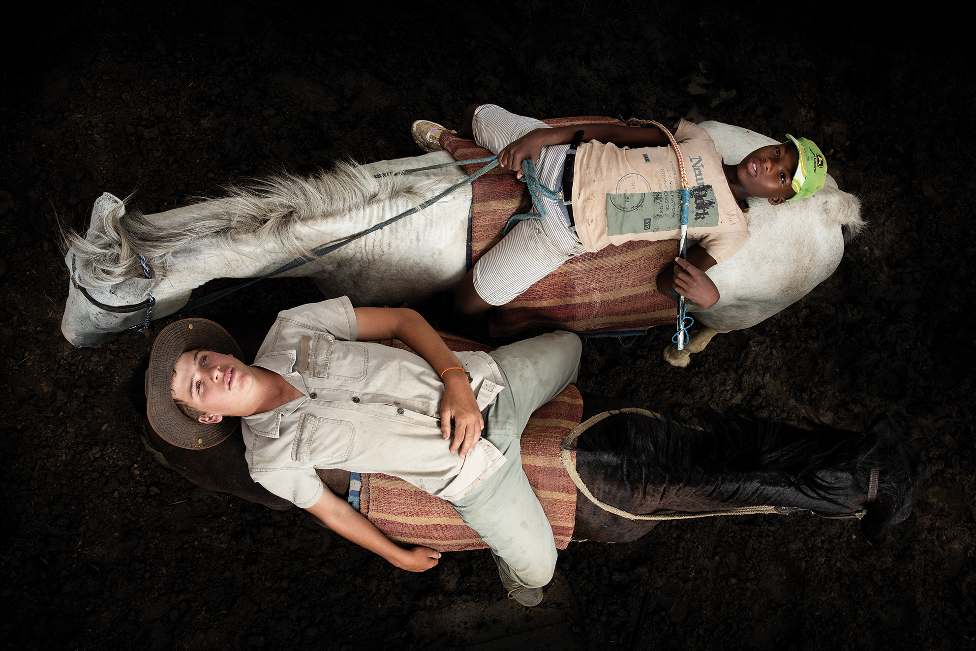 Two boys lie on horses in relaxed poses on a dark ground