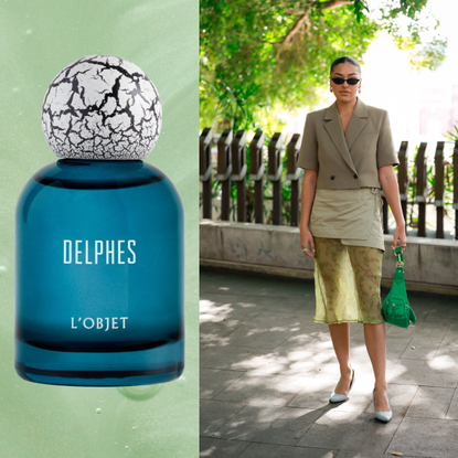 A woman wearing a monochromatic green outfit next to a bottle of olive perfume. 