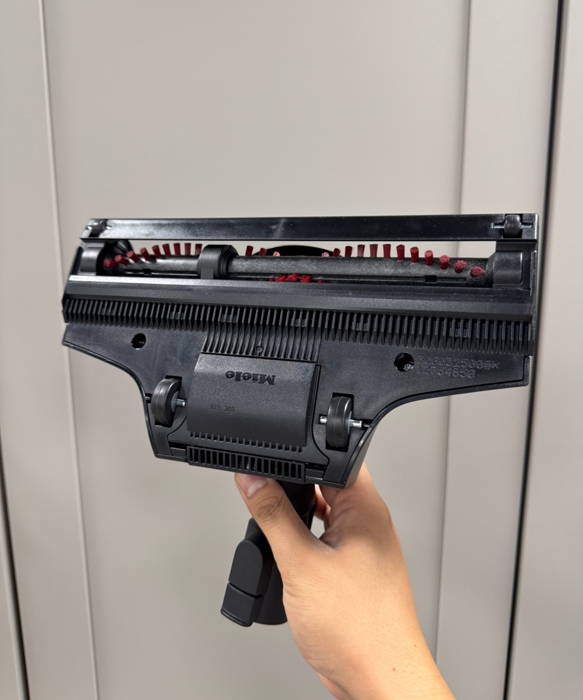 Hand holding the Miele Guard L1 Cat and Dog canister vacuum's TurboTeQ floorhead in front of gray cabinets.