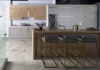 A modern kitchen with marbled flooring, an island, and cabinets with gold edging