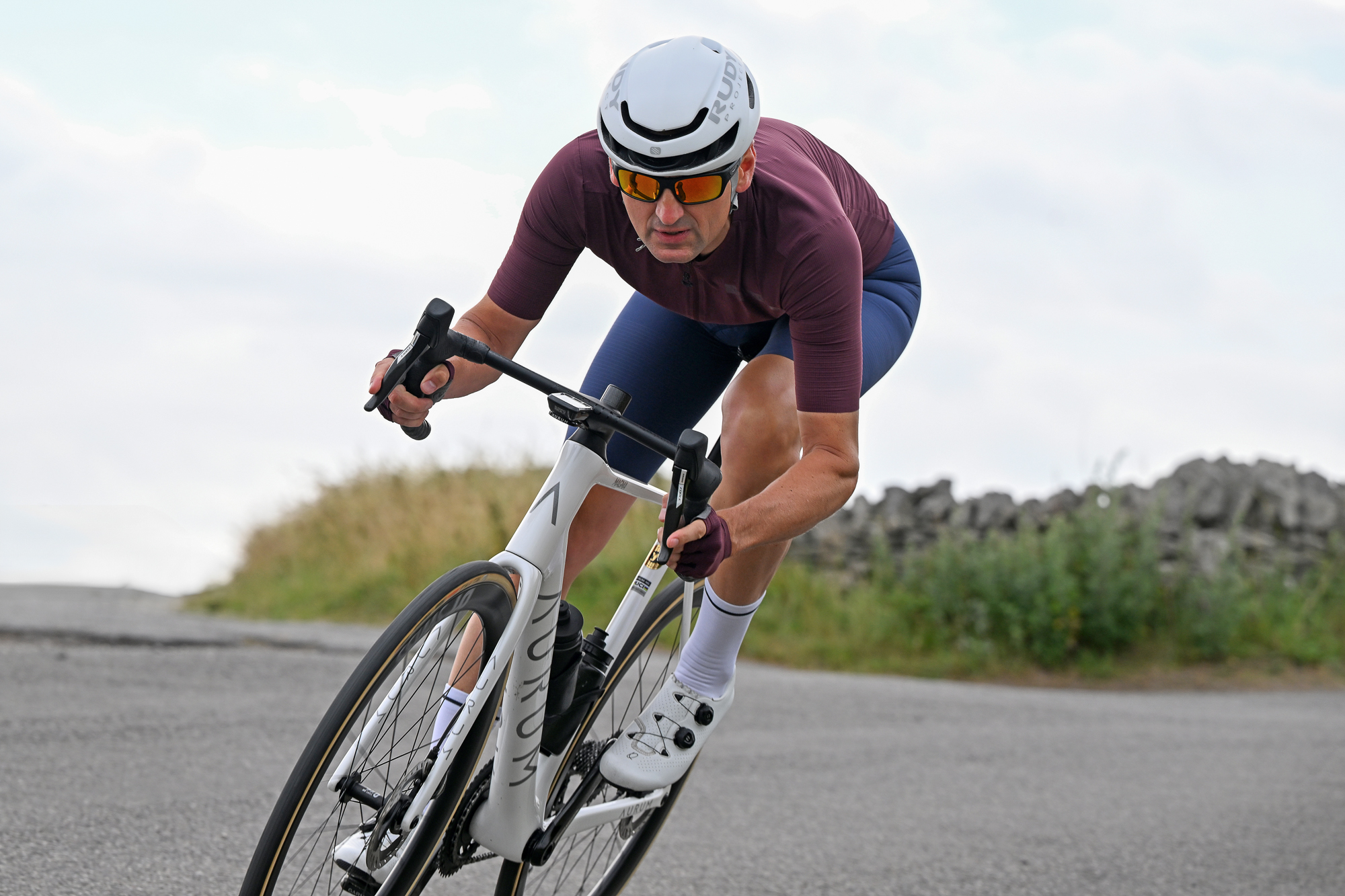 man riding a bike downhill round a corner wearing a purple jersey and white helmet