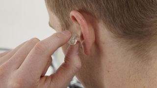 A musician inserts an earplug into his left ear