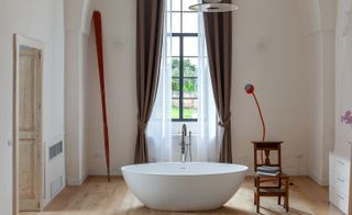 Bathroom featuring free-standing bath, wooden chair with towels, red floor lamp and window looking into the garden