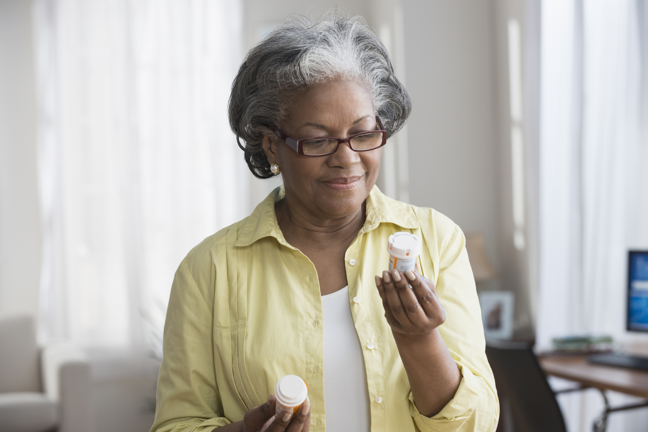 Older black woman sitting on a chair holding two pill bottles. 