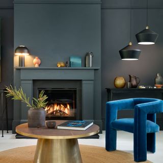 blue living room with a blue velvet sculptural armchair and gold coffee table tanle lamp on the mantelpiece and pendant lighting over the chair