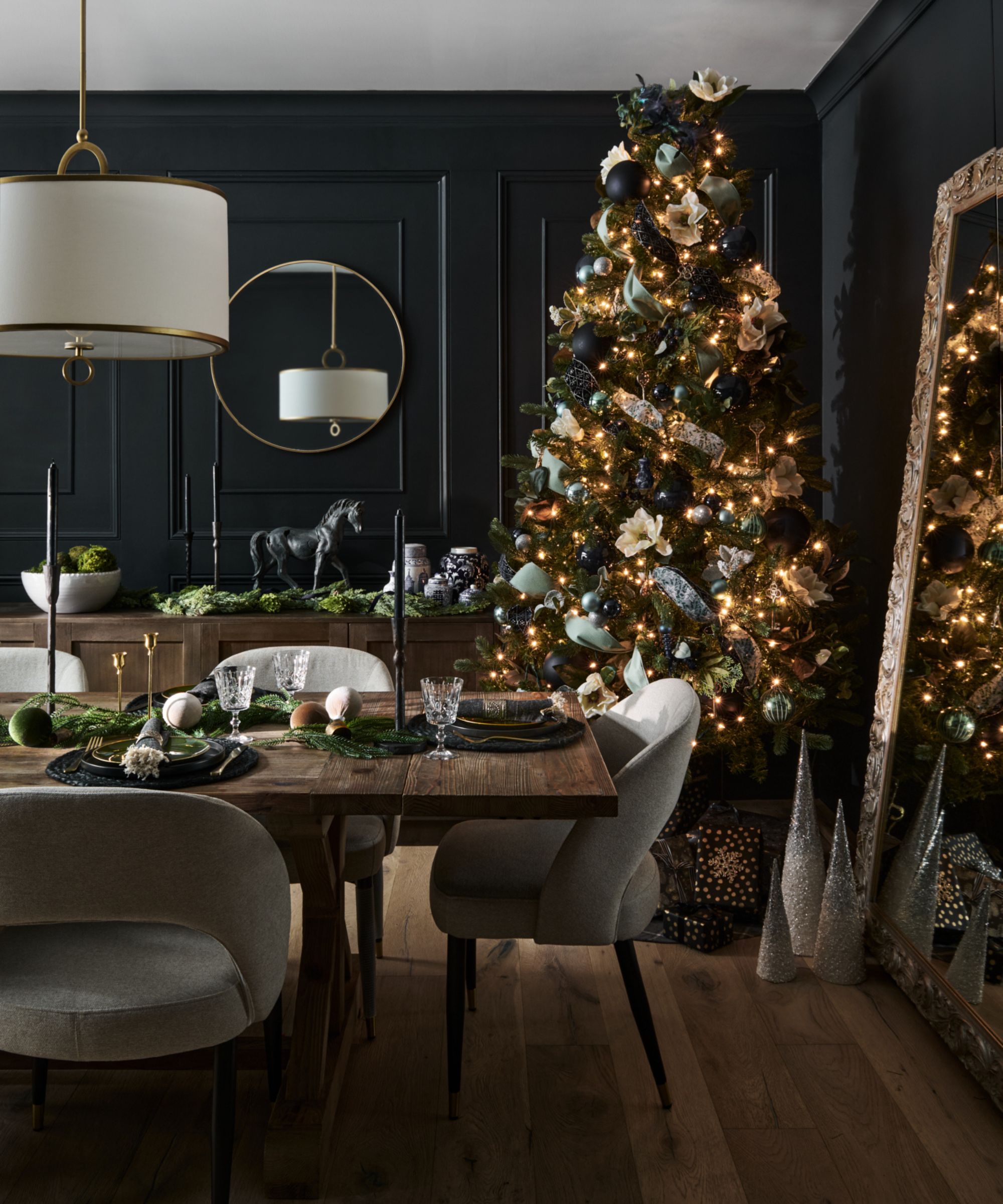 A dark dining room with black panelled walls, a Christmas tree, a dark wooden table and grey seats
